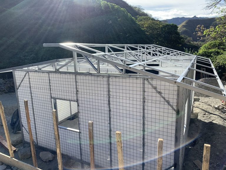 The same workshop under construction, its welded-wire panels standing with the steel roof frame above